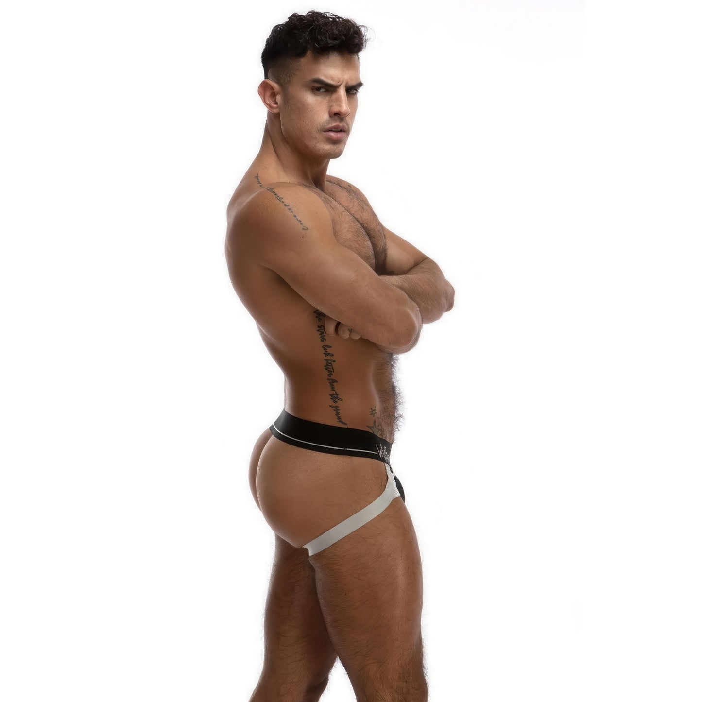 A muscular tattooed man poses in profile against a white background, wearing the *ssTricks Juku Jock in Chrome with a satin elastic band.