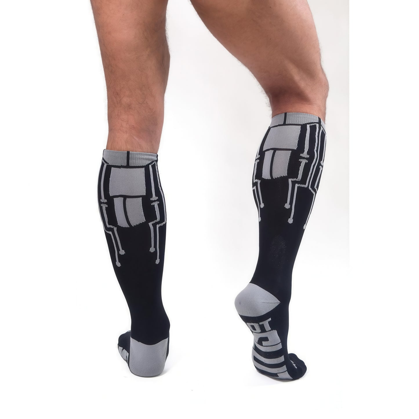 A person stands on a white background wearing *ssTricks CyberTech Socks & Black, knee-high socks featuring a gray geometric, tech-inspired circuit design on the back.
