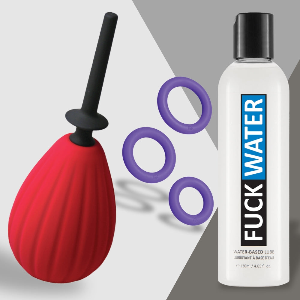 The Date Night Disaster Fixer from Adams Toy Box featuring a red bulb enema with a black nozzle, three purple silicone cock rings, and a bottle of Fuck Water lube rests on a light gray background.