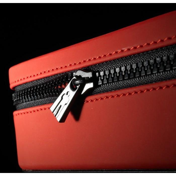 A close-up shows the Male Edge Pro Penis Enlarger Kits red zippered case, featuring a metallic zipper against black tape. It sits on a black background highlighting its sleek design and innovative traction technology.