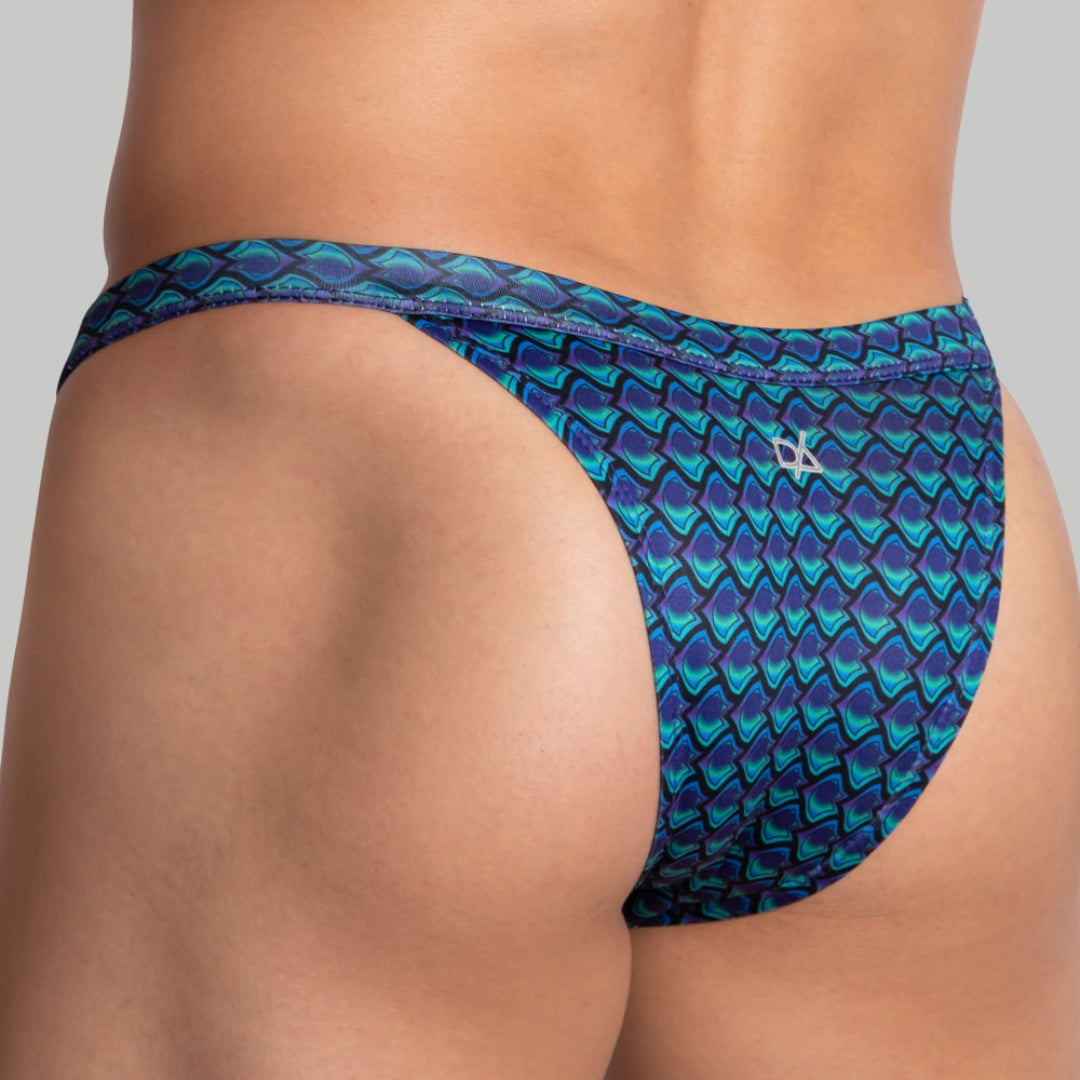 Close-up of a person’s lower back and hips wearing a blue and green patterned swimsuit brief with a geometric design, set against a plain gray background.