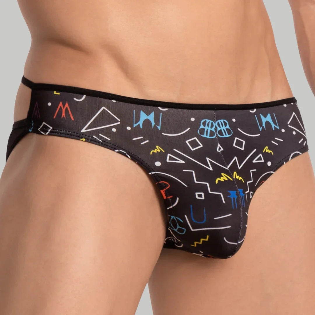 A close-up of a person wearing black briefs with colorful geometric and abstract patterns, including triangles, circles, and squiggles, on a light gray background.