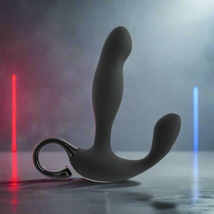The Playboy Pleasure Come Hither Prostate Massager - 2 AM, in black body-safe silicone with a looped handle, is displayed on a reflective surface. The backdrop glows in misty hues under red and blue lighting.