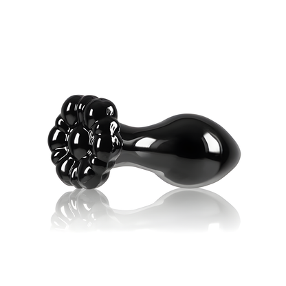 The Crystal Flower Butt Plug by NS Novelties features a glossy black finish resembling a blooming flower with a smooth, bulbous handle. Its reflective surface, similar to borosilicate glass, beautifully catches the light against a white background, showcasing elegant and versatile shapes.