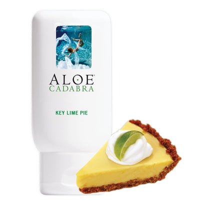 An Aloe Cadabra Organic Lubricant bottle, enriched with aloe vera and labeled Key Lime Pie, sits beside a key lime pie slice topped with whipped cream and lime, highlighting its glycerin-free formula.