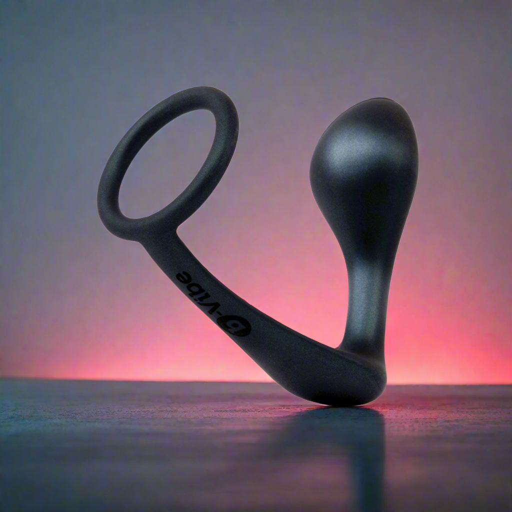 Displayed on a gradient of pink and gray, the b-Vibe Butties Ringer Cock Ring & Prostate Plug by b-vibe features a sleek black design with a curved shape and loop handle for dual action stimulation.