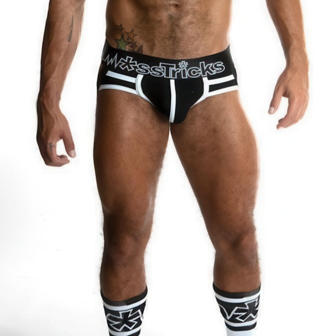 A muscular male model wears *ssTricks Juku Jock - Monochrome black and white briefs and matching geometric knee-high socks, striking a pose against a white background. His face is not shown.