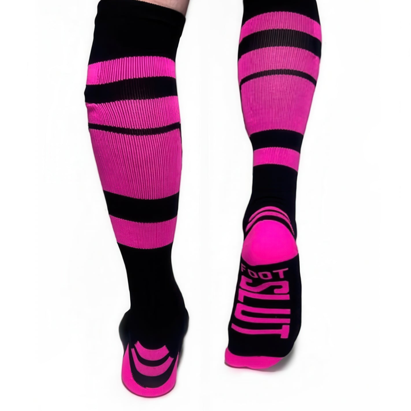 A person wears *ssTricks knee-high socks in neon pink with black stripes, featuring a cheeky FOOT SLUT on one sock bottom. Perfect for those who dare to stand out.