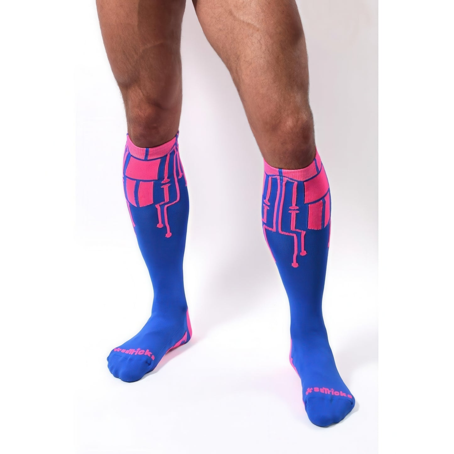A person wearing *ssTricks CyberTech Socks Neon Pink & Blue stands against a white background. The calf-length design features a pink geometric circuit pattern, neon blue base, pink toes, and bold lettering for a futuristic tech-inspired look.