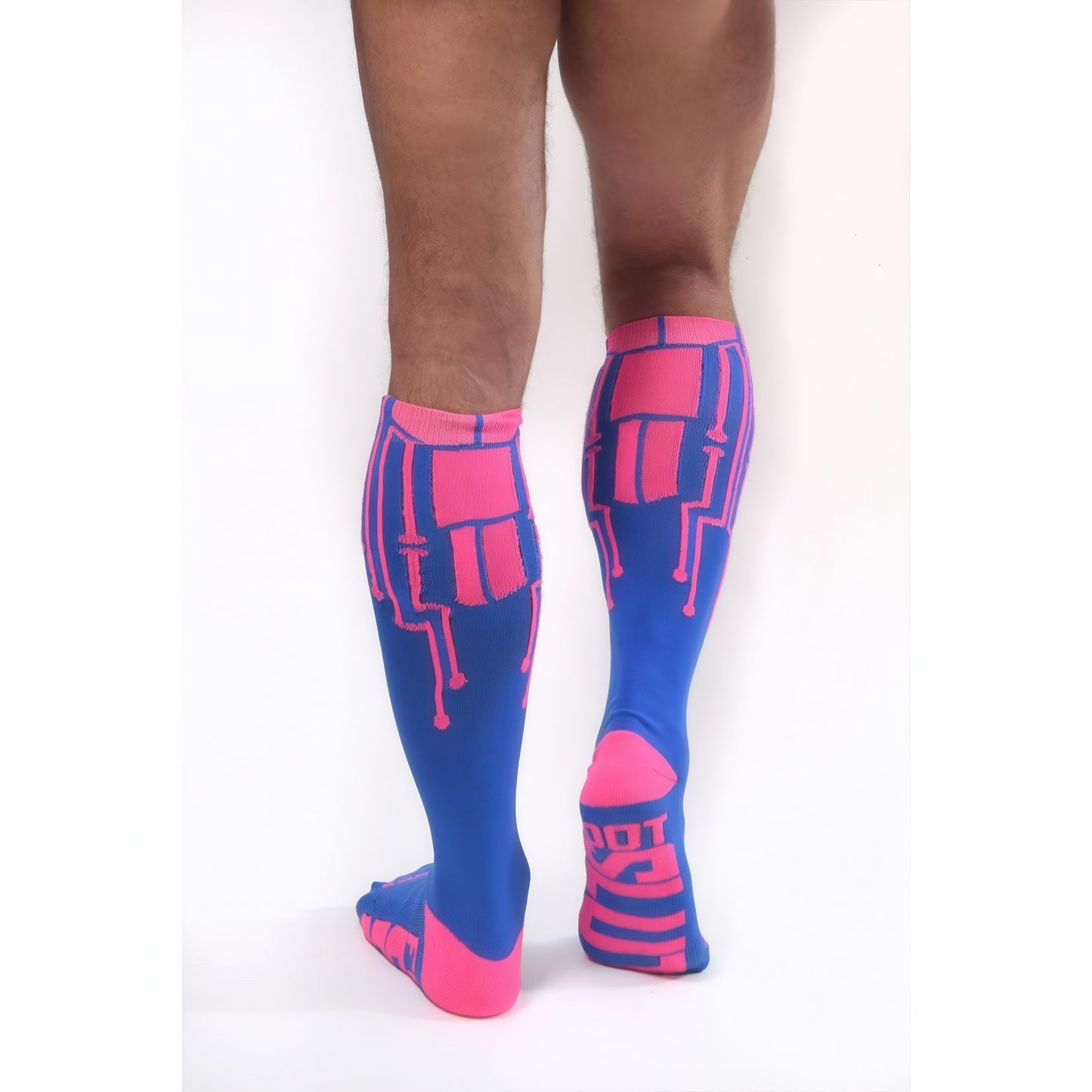 A person stands on a white background, viewed from the back, wearing *ssTricks CyberTech Socks Neon Pink & Blue—knee-high compression socks with pink circuit-like patterns and accents for a futuristic tech-inspired look.