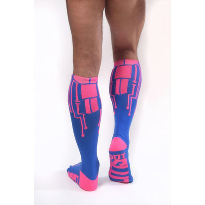 A person stands on a white background, viewed from the back, wearing *ssTricks CyberTech Socks Neon Pink & Blue—knee-high compression socks with pink circuit-like patterns and accents for a futuristic tech-inspired look.