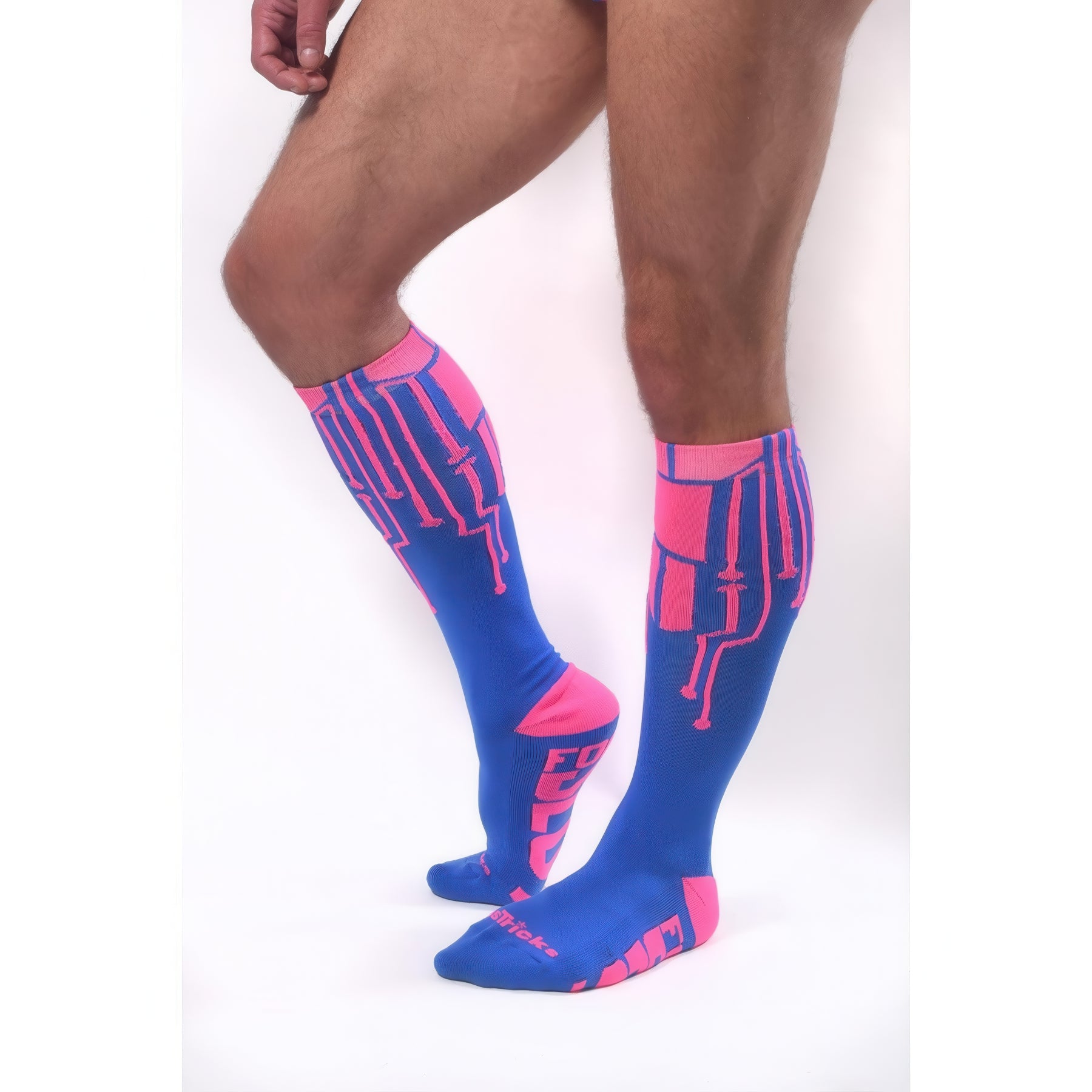 A person wearing *ssTricks CyberTech Socks Neon Pink & Blue stands on tiptoes against a white background, showcasing only their legs and the socks’ striking neon pink circuit designs on blue for a futuristic tech-inspired look.