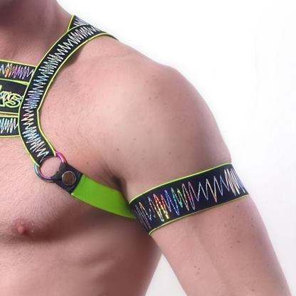 A person models the *ssTricks Electro Arm Bands in Neon Green, paired with a vibrant zigzag-patterned harness featuring metallic rings, highlighting the accessories on their shoulder and chest.