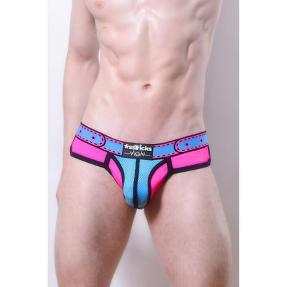 A shirtless male torso models the *ssTricks Comicaze Brief Pink & Blue, featuring neon pink and blue breathable mesh, black trim, and a patterned waistband. The white background highlights these bold superhero-inspired briefs.