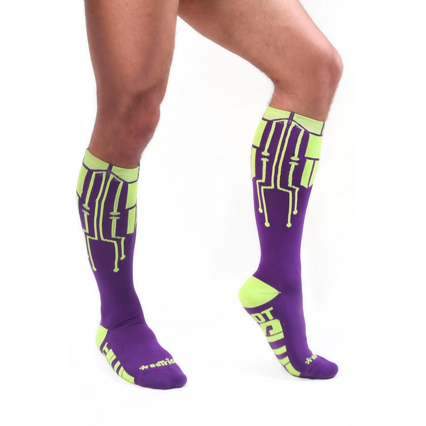 A person models *ssTricks CyberTech Socks Neon Yellow & Purple, featuring neon circuit-inspired designs, standing on one leg against a white background to showcase their futuristic tech style.