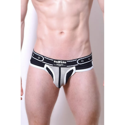 A person wearing Comicaze Brief Black & Grey underwear by *ssTricks, featuring a belt-like design and bold branding on the waistband, poses against a plain light background.