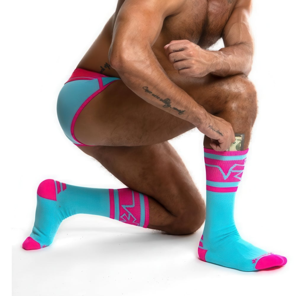 A person kneels, wearing *ssTricks Cotton Candy socks with hidden pockets and matching briefs. Their right hand adjusts the sock on the left leg; the background is white.