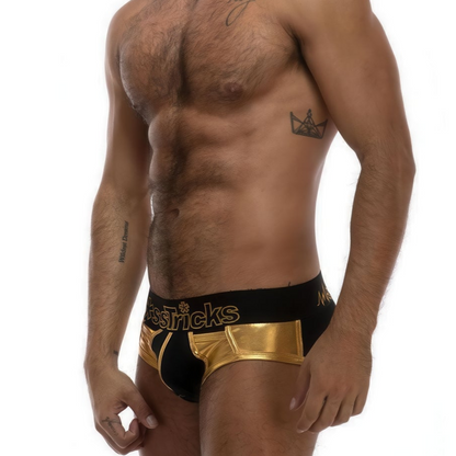 A male model showcases *ssTricks Pocket Brief in Golden Glory, featuring a black and gold design with bold waistband lettering. Complementing his tattooed arm, his side pose highlights the sleek style and craftsmanship of this underwear.