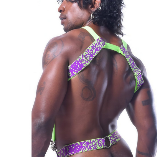 A person with long hair faces away, showing a muscular back adorned in the PIXELATION HARNESS by *ssTricks. This neon green/purple reversible design features shoulder-crossing straps and a waist encirclement, with tattoos adorning the arms and shoulders.