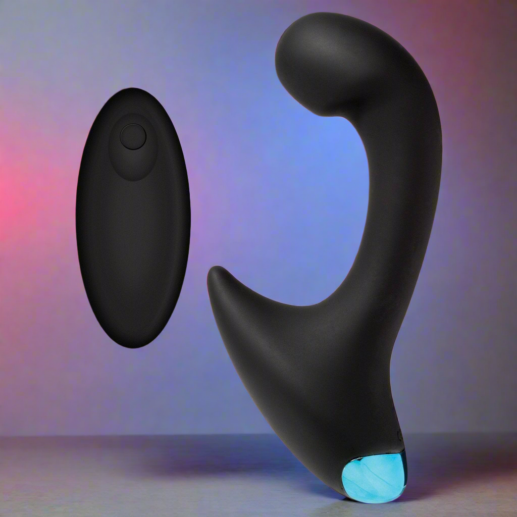 Adams Toy Boxs black OptiMale Vibrating P Massager with Wireless Remote, featuring a glowing blue tip and waterproof design, is set against a gradient backdrop transitioning from pink to blue hues. A floating black remote with one button complements the scene.