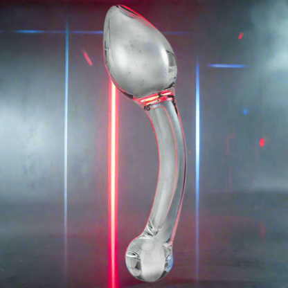 The Gläs Pure Indulgence Anal Prostate Toy by Gläs, a transparent hand-blown glass object, stands upright on a reflective surface with red and blue neon lights in the background, creating a futuristic vibe ideal for P-spot stimulation.