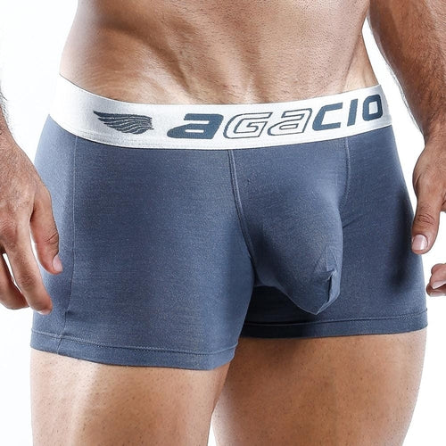 A close-up of a person in Agacio Boxer Trunk, featuring a blue design with a white AGACIO waistband and wing logo. The silky smooth fabric and contour pouch accentuate the torso and upper legs, offering comfort and style.