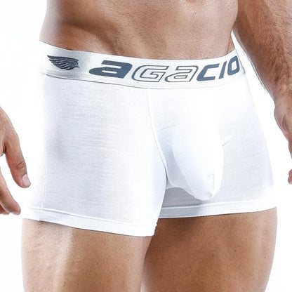 A person wearing white Agacio Boxer Trunk stands against a neutral background, showcasing the contouring pouch, silky smooth fabric, and logo on the waistband.