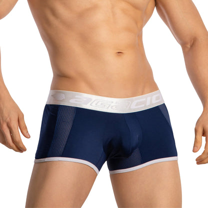 A person wearing Agacio Boxer Sheer Trunks in navy blue with a white waistband and light blue accents focuses on the midsection, highlighting the contoured support and stylish design.