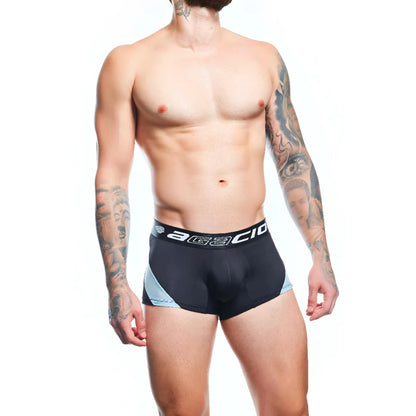A tattooed man models Agacio Boxer Trunks Comfortable Underwear in black, with a waistband displaying white lettering. The premium fabric blend and contour pouch are highlighted against a plain white background.