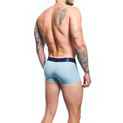 A tattooed man confidently poses against a white backdrop, highlighting the comfort and support of his light blue Agacio Boxer Trunks Comfortable Underwear with a dark waistband.