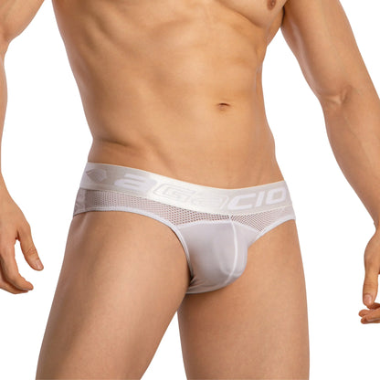 A man poses against a plain background, showcasing the Agacio Mens Sheer Brief made from luxurious fabric featuring mesh details on the waistband and sides, revealing his toned torso.