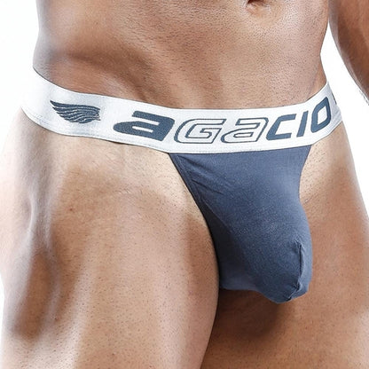 A close-up image features someone in the Agacio Slip Thong, navy blue with a white waistband. Agacio is printed boldly on the band, emphasizing its sexy design and enhancing pouch for added appeal.