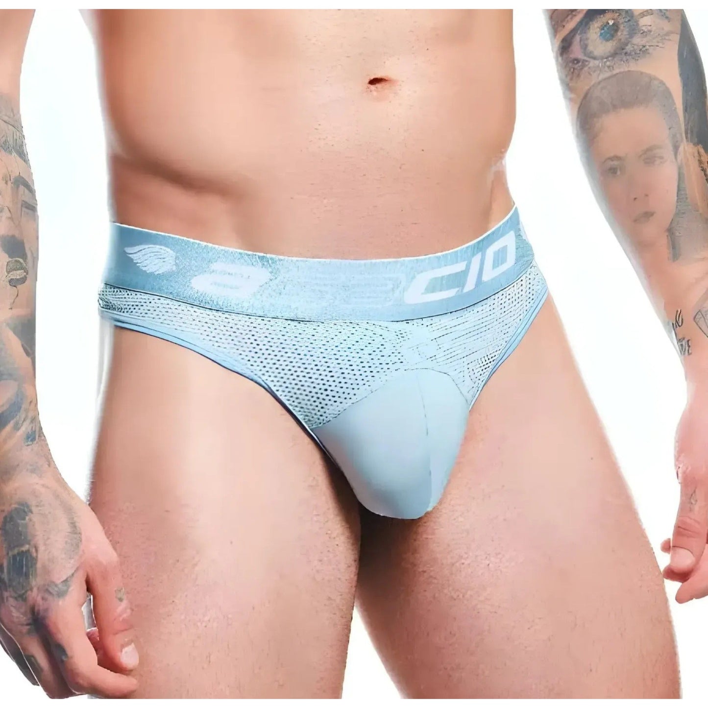 A person with arm tattoos showcases a minimalist design wearing the pale blue Agacio Thong for Men. The waistband features the Agacio logo, complementing the premium fabric blend that ensures comfort and style.
