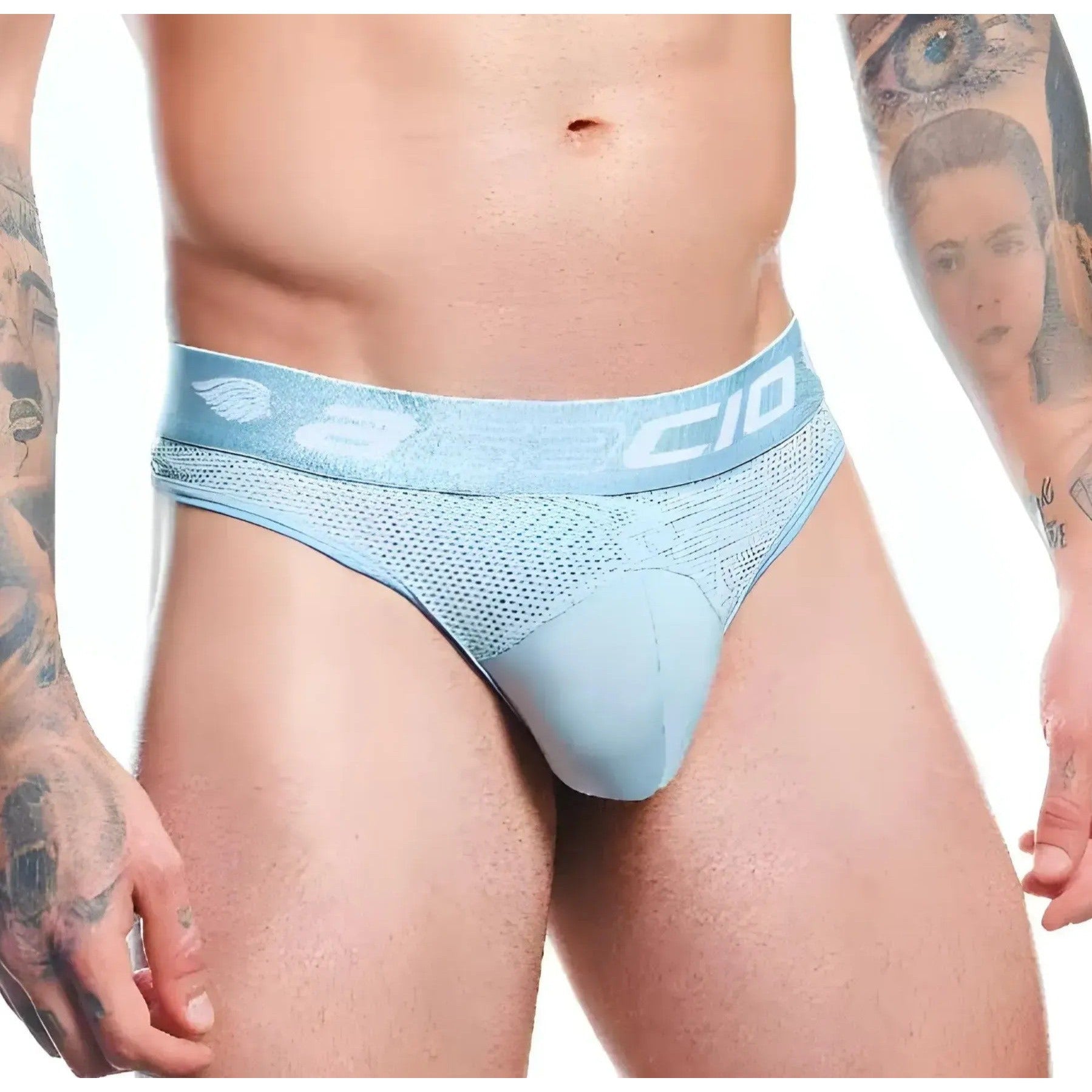 A person with arm tattoos showcases a minimalist design wearing the pale blue Agacio Thong for Men. The waistband features the Agacio logo, complementing the premium fabric blend that ensures comfort and style.