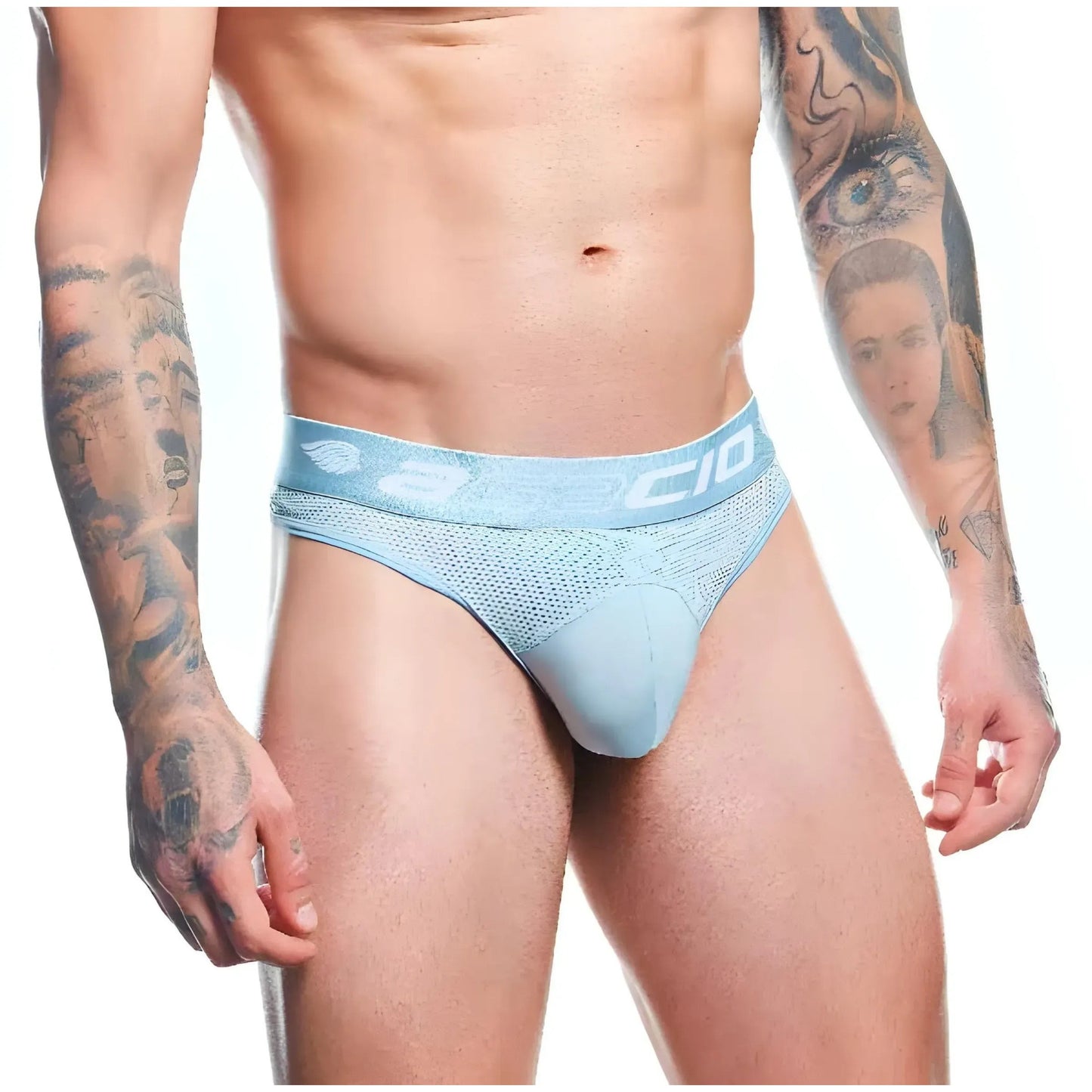 A person in Agacio Thong for Men, crafted from a premium fabric blend, stands hands at sides against a white background. Tattoos of faces and abstract designs on their arms and torso contrast strikingly with the minimalist underwear design.