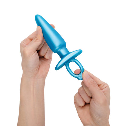 Two hands hold the b-Vibe Butties Sleek Tapered Plug by BV-075 in vibrant blue. Made from body-safe silicone, it features a tapered end and looped handle for grip and ease. The white background highlights its striking color, ideal for comfortable anal training.