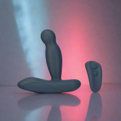 The Lux Active Revolve 4.5 Rotating & Vibrating Anal Massager by LUX and its matching remote are shown on a reflective surface, set before a soft blue, pink, and red gradient backdrop.
