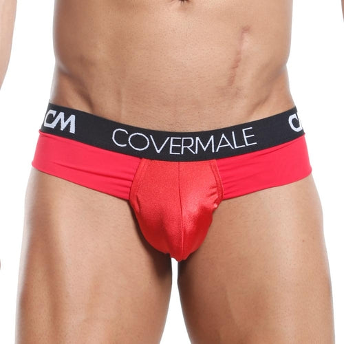 A person models the Cover Male Slip Thong, a stylish red brief with a black waistband and COVERMALE in white. The smooth, shiny fabric offers cheeky coverage for a modern look while highlighting the lower torso.