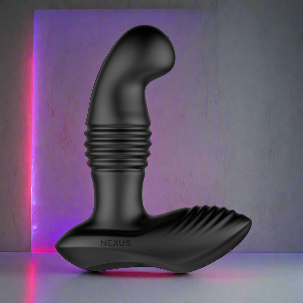 The Nexus Thrust Prostate Edition by Nexus is a black prostate massager with a ridged design, spotlighted against a textured gray background. A pink and purple hue glows from the top left corner, highlighting its sleek matte finish. This remote control device offers multiple vibrating modes.