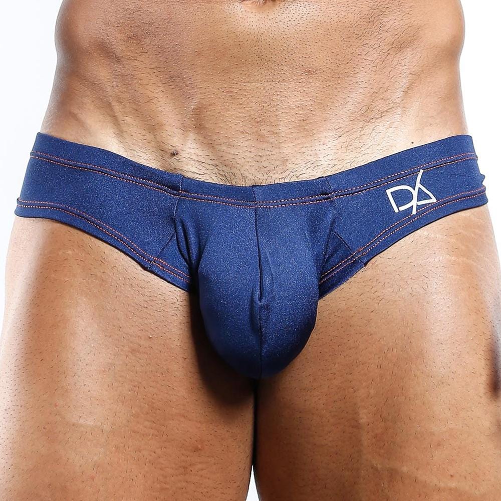 A close-up shows someone wearing Daniel Alexander Emotion Slip Thong in navy blue, with a logo on the waistband and red stitching details. The focus is on the midsection, highlighting the premium design and fit.