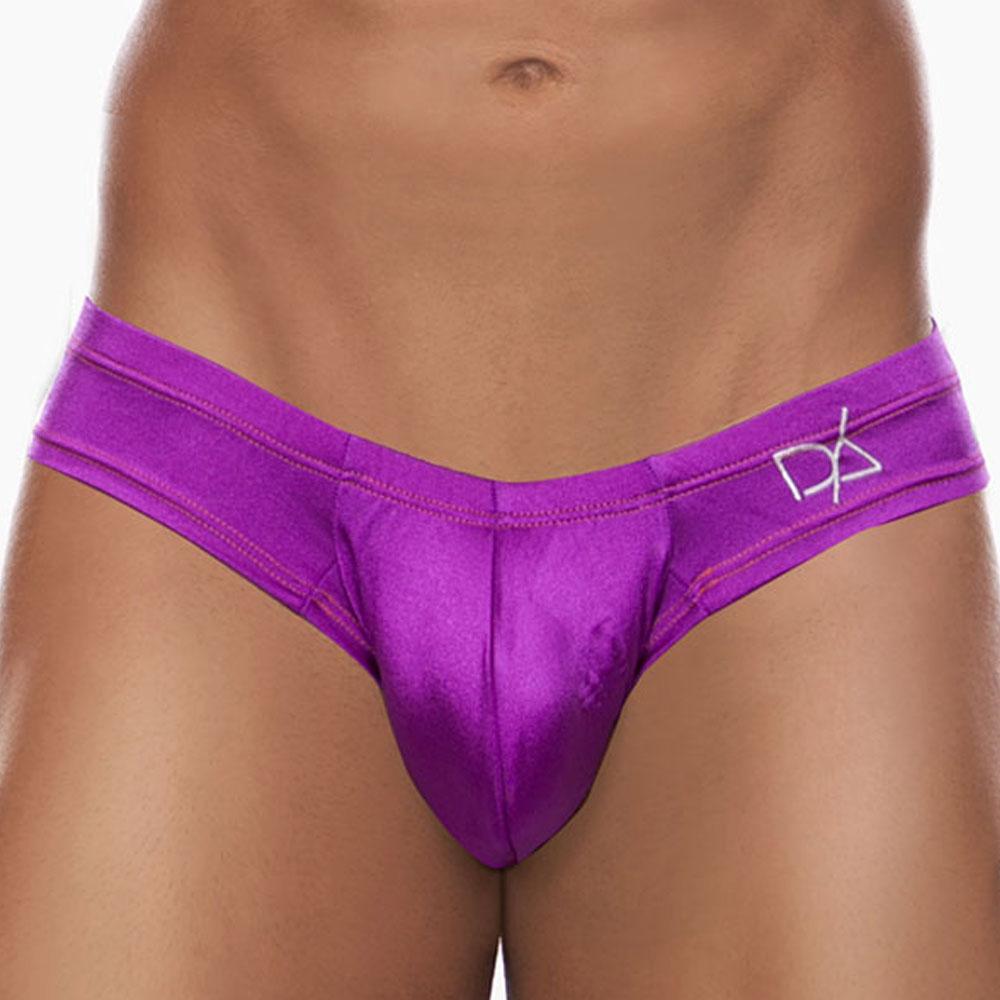 A person stands against a plain background wearing the Daniel Alexander Emotion Slip Thong in bright purple with a cheeky back design and a small logo. Made from a premium fabric blend, the thong has a shiny, satin-like texture. Only the midsection is visible.