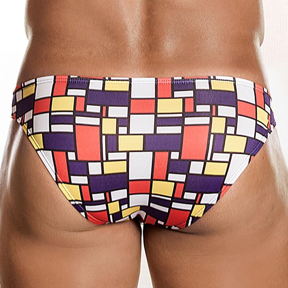 A person with their back to the camera wears Daniel Alexanders vibrant Art-Deco Fritz Bikini Brief, showcasing bold geometric prints in red, yellow, black, and white against a plain white wall.