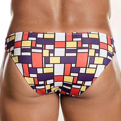 A person with their back to the camera wears Daniel Alexanders vibrant Art-Deco Fritz Bikini Brief, showcasing bold geometric prints in red, yellow, black, and white against a plain white wall.