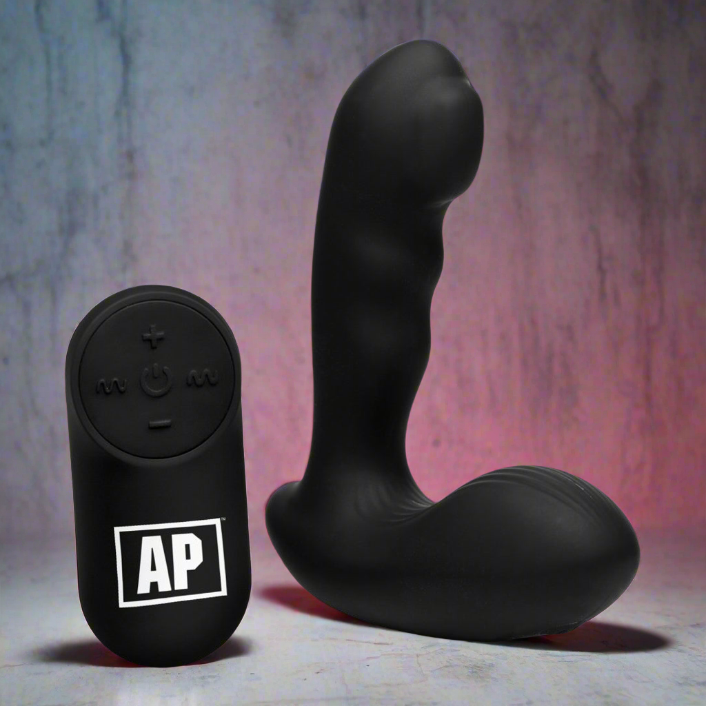The Alpha Pro 7x P-Milker Prostate Stimulator With Milking Bead, made from premium black silicone, elegantly rests on a surface against a pink and gray backdrop. It features a remote with plus, minus, and power symbols along with AP, enhancing your experience effortlessly.