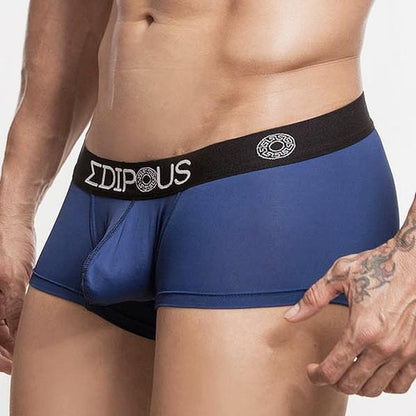 A person wearing Edipous Eros Short Boxer, featuring a black waistband with the logo and text, is shown with their torso and tattooed arm partially visible against a plain background.