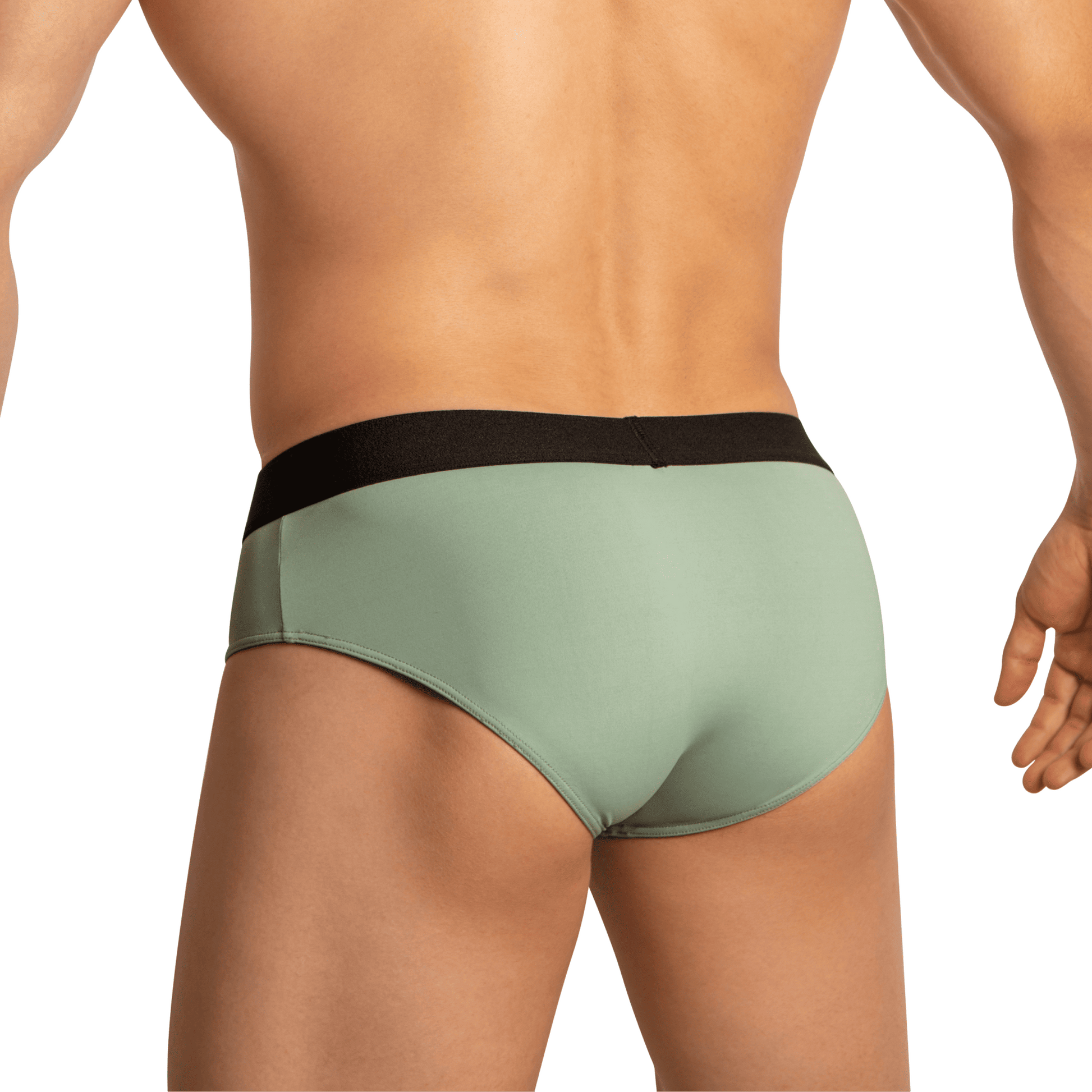 A person models Edipous Briefs for Men Open Front, featuring light green fabric and a black waistband, as seen from behind. The plain background accentuates the alluring fit and style of this underwear by Edipous.