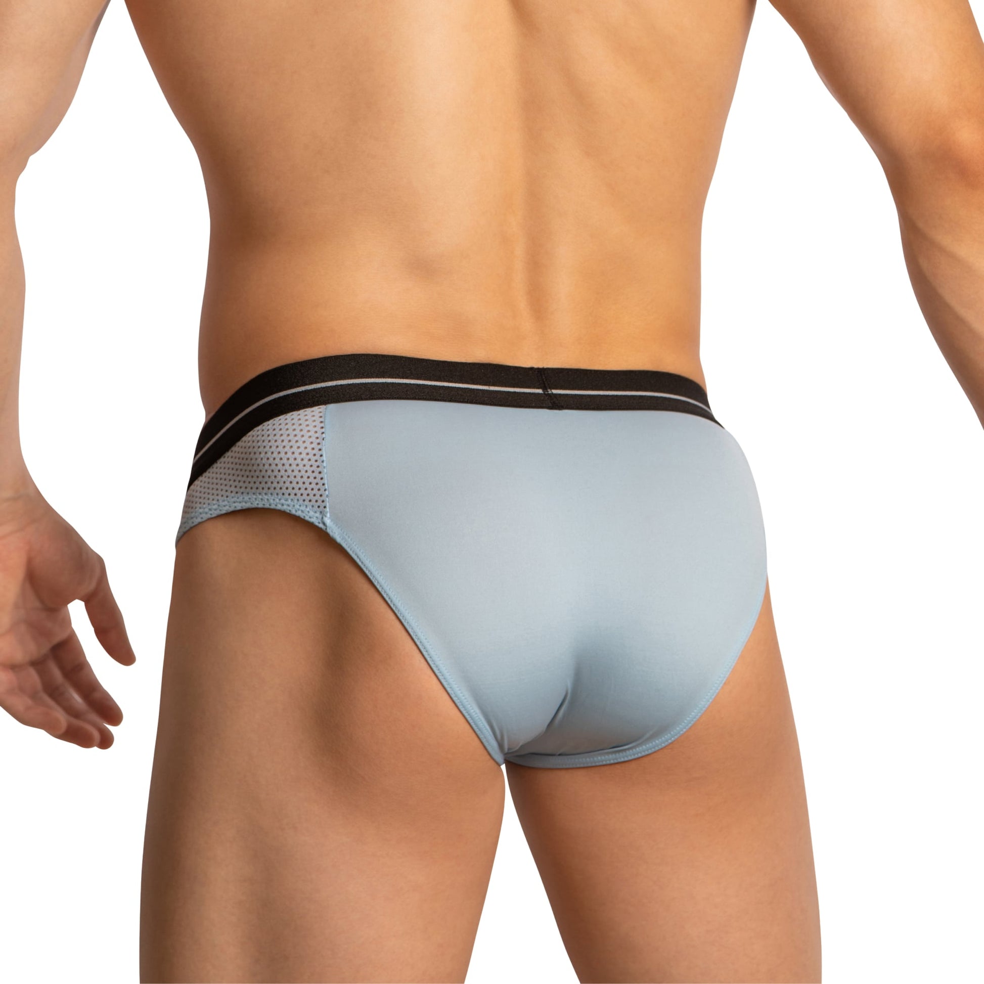 The image shows a person from behind in Feel Thongs for Guys, featuring light blue fabric with a black waistband and mesh side panels. Against the white background, their light skin emphasizes the stylish comfort that Feel is known for.