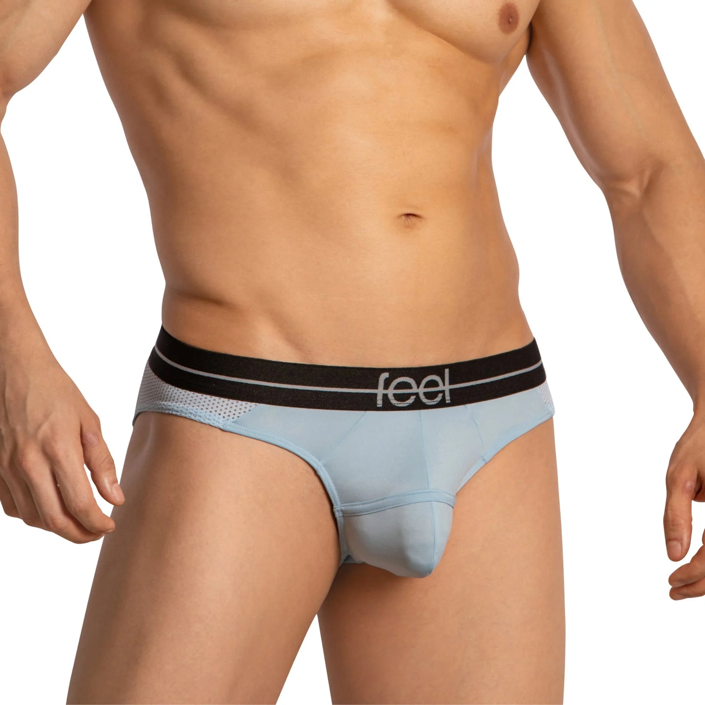 A person is wearing Feel Thongs for Guys by Feel, characterized by light blue fabric, a black waistband with Feel in white, and mesh side detailing. The persons torso appears in the shot while their head remains out of the frame.