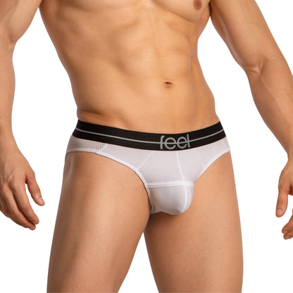 A male model showcases Feel Thongs for Guys from Feel, featuring a snug fit and sleek design. The white thongs with a black waistband branded with feel highlight both style and comfort while subtly emphasizing the elegance of his torso and upper legs.