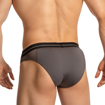 A person is seen from the back wearing Feel Thongs for Guys in gray, featuring a black waistband and mesh side panels, merging style and comfort. They stand against a plain white backdrop, highlighting the sleek design.